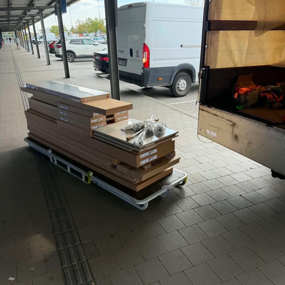 Lapraszerelt bútorok dobozai egy áruházi kocsin, mellettük a CuccTaxi nyitott teherautója